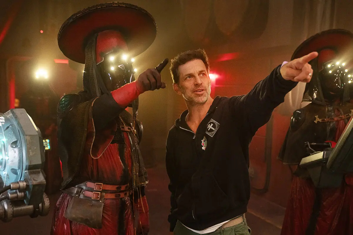 Director Zack Snyder on the Rebel Moon set between two finished Imperium medical technicians in red robes